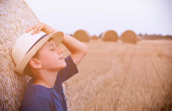 Yaz aylarında gün batımında haystacks yakınındaki şapkalı çocuk genç sevimli ülke. Yaz kavramı, bir tatil. Etkin açık havada eğlence sıcak yaz gününde çocuklu.