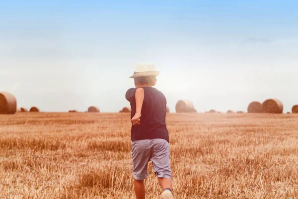 Молодий симпатичний сільський хлопчик в капелюсі поблизу сіна на заході сонця влітку концепція, відпустка. Симпатичний хлопчик сидить на сідловині — стокове фото
