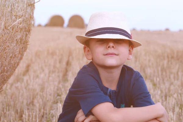 Young cute country boy in hat near haystacks at sunset in summer. Summer concept, a vacation.Active outdoors leisure with children on warm summer day. — Stock Photo, Image