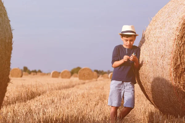 Młodych cute kraju chłopca w kapeluszu w pobliżu Stogi o zachodzie słońca latem. Koncepcja lato, wakacje. Na zewnątrz aktywny wypoczynek z dziećmi na ciepły, letni dzień. — Zdjęcie stockowe