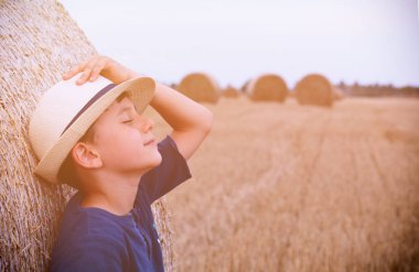 Yaz aylarında gün batımında haystacks yakınındaki şapkalı çocuk genç sevimli ülke. Yaz kavramı, bir tatil. Etkin açık havada eğlence sıcak yaz gününde çocuklu.