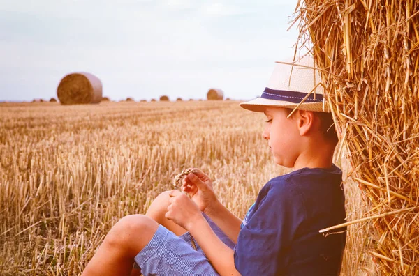 Joven chico de campo lindo en sombrero cerca de pajar al atardecer en verano. Concepto de verano, unas vacaciones.Activo ocio al aire libre con los niños en el cálido día de verano . —  Fotos de Stock