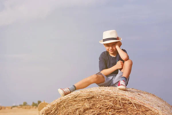 Cute chłopiec siedzi na stogu siana. Na zewnątrz aktywny wypoczynek z dziećmi na ciepły, letni dzień. Koncepcja lato, wakacje. — Zdjęcie stockowe