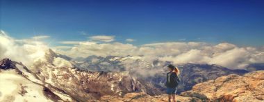 Woman standing on a mountain top  above the cloudy valley.Panorama. clipart