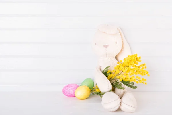 Белый кролик с мимозой и пасхальными яйцами — стоковое фото