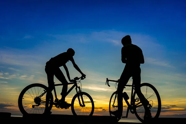 Cyklisté s koly na pláži, za soumraku. — Stock fotografie