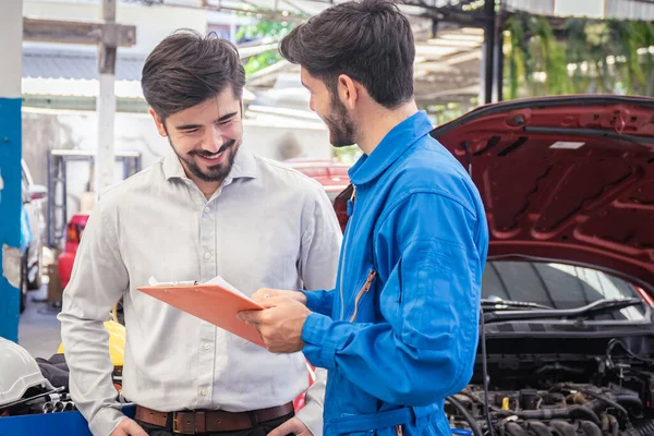 Mechanic holding clipboard with car owner in the workshop garage. Car auto services concepts