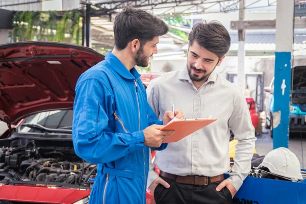 Mechanic holding clipboard with car owner in the workshop garage. Car auto services concepts