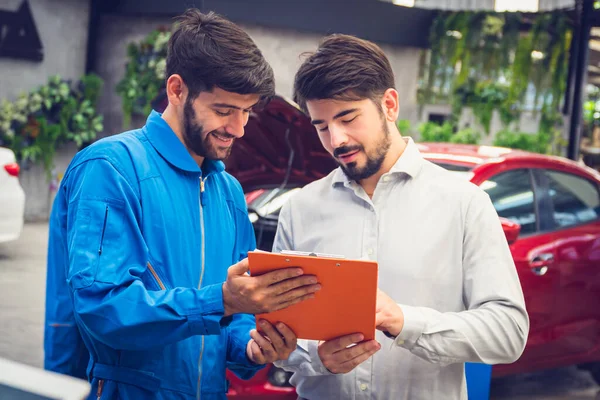 Mechanic holding clipboard with car owner in the workshop garage. Car auto services concepts