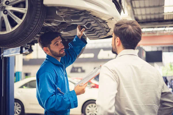 Mechanic holding clipboard with car owner in the workshop garage. Car auto services concepts