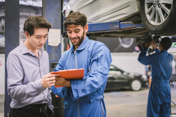 Tamirci, tamirhanenin garajında araba sahibiyle birlikte pano tutuyor. Otomobil servisi kavramları