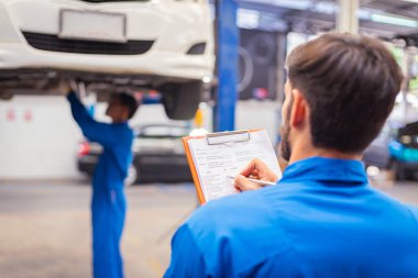 Tamirci arabayı kontrol ediyor ve kağıda not alıyor. Otomobil servisi kavramları