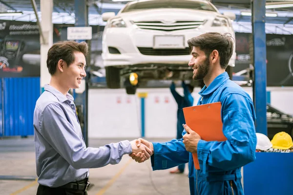 Tamirci atölye garajında araba sahibiyle el sıkışıyor. Otomobil servisi kavramları