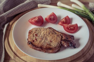 Domuz biftek, beyaz bir tabağa dilimlenmiş domates sarımsak bir ahşap tepsi, sığ derinlik-in tarla, vintage etkisi yeşil Genç sürgünler
