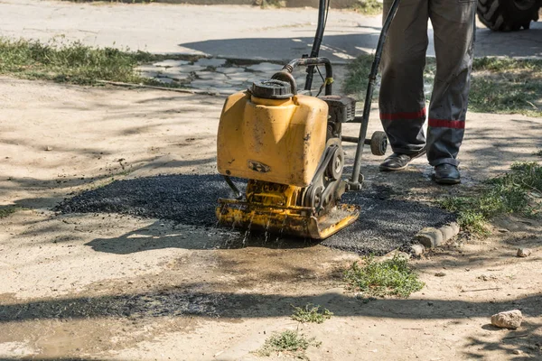 Road repair details. A worker with a manual paver aligns the hot asphalt on the road.