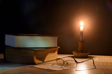 Masanın üzerindeki kitaplar loş mum ışıkları tarafından aydınlatıldı. Masanın üzerinde loş mum ışığı yakıldı.