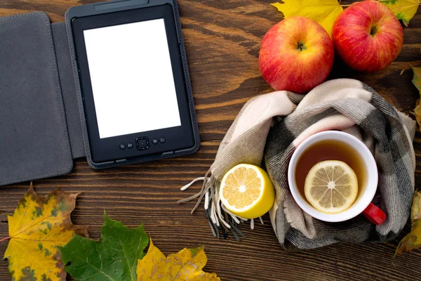 Ebook en een kop hete thee met een citroen verpakt in een sjaal op een houten tafel — Stockfoto