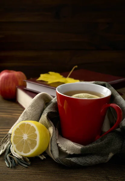 Une tasse de thé chaud au citron, enveloppé dans une écharpe sur une table en bois avec des feuilles jaunies et une pile de livres — Photo