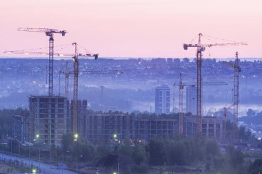 Kule vinçleri, gün batımında ya da gün doğumunda kentteki bir inşaat alanında yeni bir apartman inşaatı. Kârlı yatırımlar ve yenileme programı, geliştirme, inşaat endüstrisi konsepti