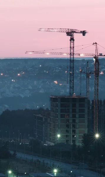 Tower cranes, the construction of a new tall apartment building at a construction site in the city at sunset or sunrise. Profitable investments and renovation program, development, construction industry concept