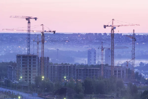 Tower cranes, the construction of a new tall apartment building at a construction site in the city at sunset or sunrise. Profitable investments and renovation program, development, construction industry concept