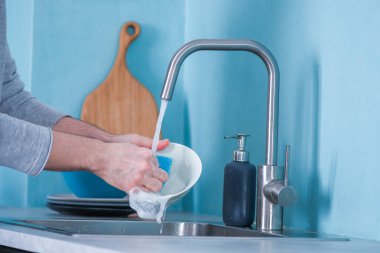 Bir adam mutfakta bulaşıkları mavi duvarlı mavi bir eko süngerle yıkıyor. modern iç mekan