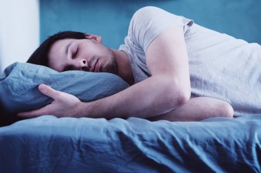 Yakışıklı adam yatak odasında tek başına uyuyor.