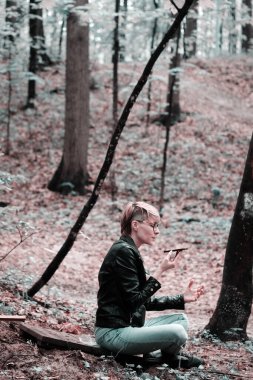 Ormanda kısa tavşanlı sarışın genç bir kadın rahatlama pozisyonunda oturuyor ve telefonla meditasyon yapıyor. Meditasyon ve ormanda çalışma