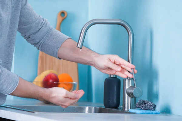 A man washes his hands before eating closeup in the kitchen on a background of blue wall next to the kitchen wash basin to wash his hands