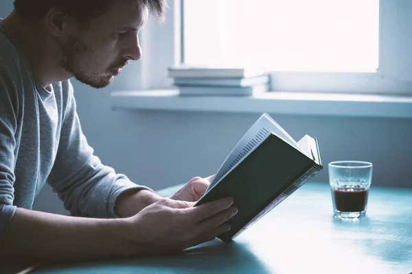 Joven Serio Hombre Sienta Una Mesa Azul Lee Libro Tensamente — Foto de Stock