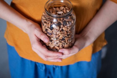 Kadın ellerinin açık cam bir fasulye kavanozunu nasıl tuttuğunun renkli renkli, yatay fotoğrafı. Yiyecek eksikliği ve çiğ vejetaryen yemeği kavramı.
