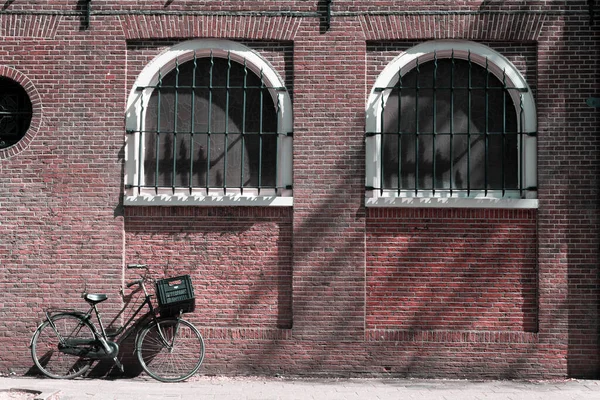 One bike is parked against an old brick wall with two large old windows
