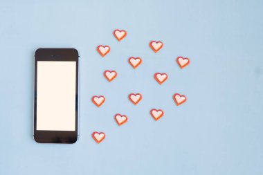 Cep telefonunun maketi kırmızı olsun, mavi arka planda kağıt kalpler olsun. İletişim konsepti, insanlar arasında flört etme.