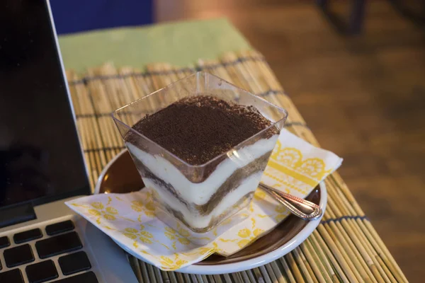 Cake "Banoffee" with caramel and banana place next to laptop in coffee shop — Stock Photo, Image