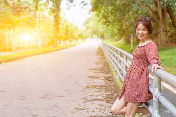 Gärna långt hår asiatisk tjej stå mot staket med leende i solen — Stockfoto