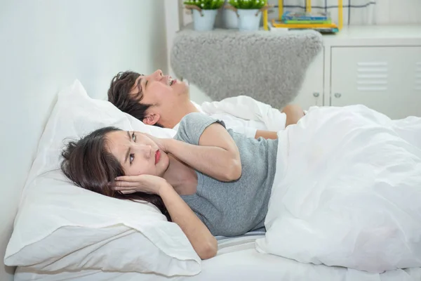 Man snoring while his wife is covering ears with the pillow.Asian young woman cover ears with pillow while her boyfriend sleep with loud snoring.