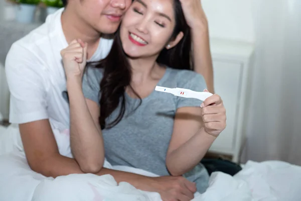 Unga glada asiatiska par med uppmuntra och krama tillsammans med graviditetstest.Förvänta mamma med glada ansikte med graviditet i händer.selektivt fokus på testare. — Stockfoto