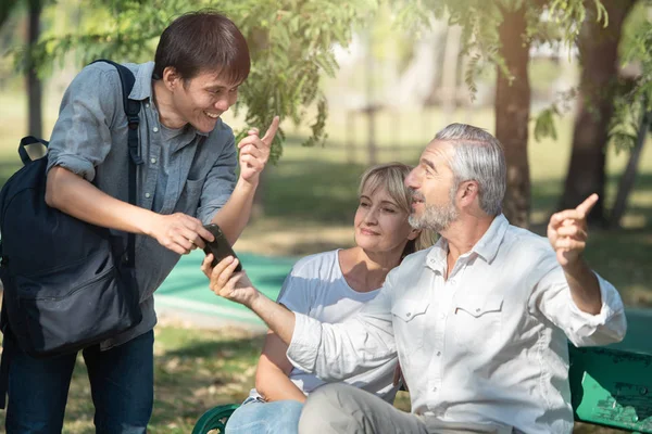 Asyalı turistler ellerinde akıllı cep telefonu olan genç bir adam bir kadınla oturan yaşlı beyaz bir adamdan yol tarifi istiyor..