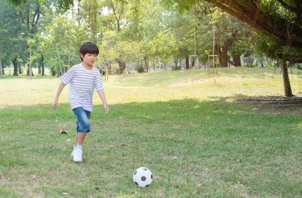 En asiatisk pojke njuter av att spela fotboll leksak i parken.Boy bär en randig vit blå skjorta. — Stockfoto