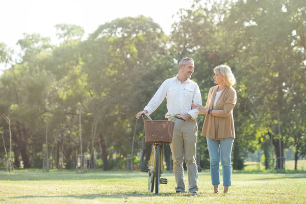 Веселая активная пожилая пара с велосипедом, прогуливающаяся по парку вместе. Идеальные занятия для пожилых людей в пенсионном образе жизни . — стоковое фото