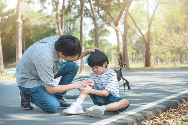 Young asian father of dad calms son that fell from the bike and he get injury on knee and leg while have weekend leisure in public park,accident can happen everywhere and every time. — 스톡 사진