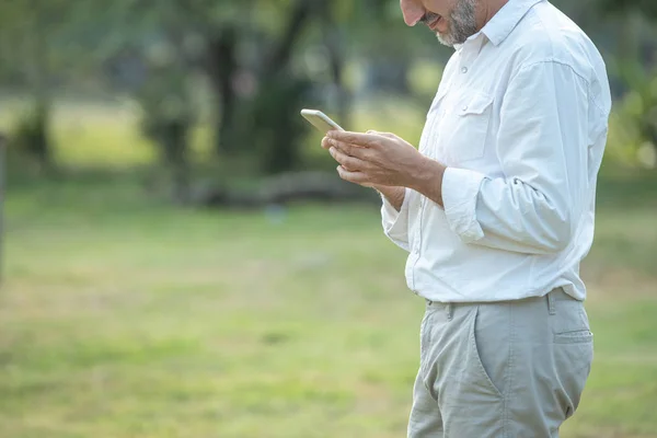 Caucásico hombre de mediana edad mano utilizando el teléfono móvil inteligente y mirar en el teléfono, mientras que el mensaje de texto en el parque, la movilidad concepto de tecnología de comunicación inalámbrica . — Foto de Stock