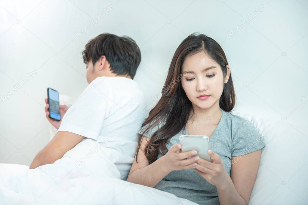 Young asian couple in bed using phone lying backs to each other.Asia man and woman use own smart mobile phone with privacy,relationship problem with technology.