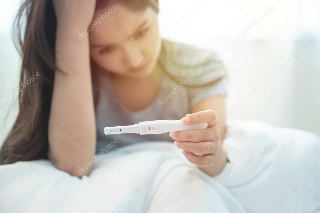 selective focus on tester.Unwanted maternity pregnant asian girl with pregnancy test in hand.Asian lady concerned and unhappy with fertility test 