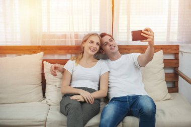 Kafkasyalı mutlu çift kanepeye oturup oturma odasında selfie çekiyorlar. Boş zamanlarında kadın ve erkeğin romantik anları..
