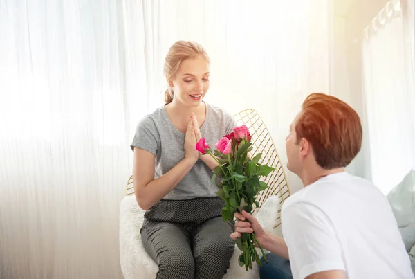 Young caucasian man sit down on knee gives bunch of roses to  woman, happiness and surprise while they having a romantic date at home,valentine concept with copy space.