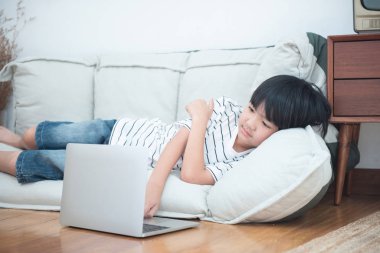 Konsantrasyonlu Asyalı çocuk laptopta oyun oynuyor. Evde kanepede yatıyor. Okuldan sonra internet kullanan mutlu bir öğrenci.. 