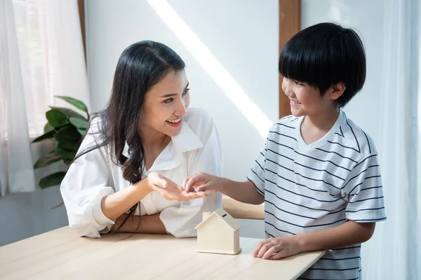 Asian son hand coin on mother palm with saving house shape container,happiness family mom and child invest for education planning finance in livingroom at home. — Stock Photo, Image