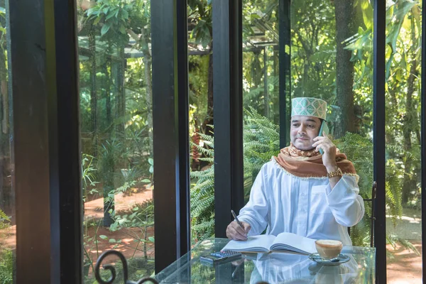 Árabe musulmán hombre de negocios utilizar la comunicación de teléfonos inteligentes y escribir en el libro en la cafetería, freelance sin estilo de vida espacio de trabajo . —  Fotos de Stock