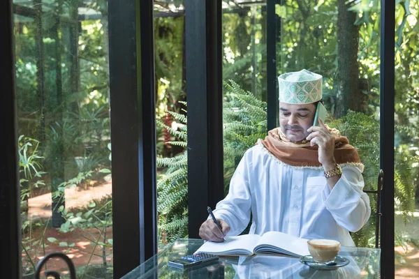 Homem de negócios muçulmano árabe usar a comunicação smartphone e escrever no livro em café, freelance sem espaço de trabalho estilo de vida . — Fotografia de Stock